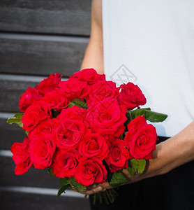 男子用一束美丽的红玫瑰花束身着白衬衫和黑裤子围着灰色木墙问候丈夫调情图片