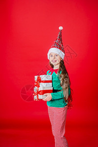 圣诞老人精灵人们十二月圣诞快乐迷人的女孩带着礼物穿鲜艳的红色亮背景上的圣诞老人助手精灵服装一个美丽的精灵婴儿肖像复制空间圣诞快乐带着礼物的快背景