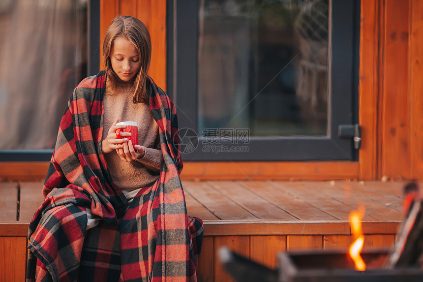 愉快在秋天温暖的日子里穿着毯裹毛的美丽女孩喝着热饮的漂亮女孩秋天在阳台上享受着秋天热的放松图片