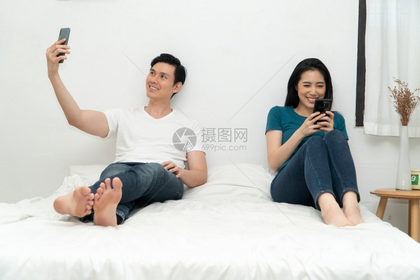 吸引人的亚洲情侣在床上时常使用智能手机但不要互相关心对方的系问题和不忠概念关系问题和不忠的概念技术时间图片