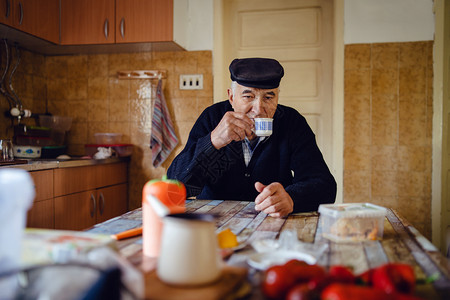养肝茶人们身着黑色毛衣和帽子在家中单坐的桌子边喝咖啡或茶的一杯高级男子曾祖父老的养金领取者背景