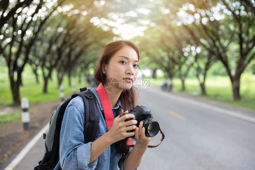爱好镜片头发女摄影师在野外拿着摄像头拍旅游者的照片来自游客图片