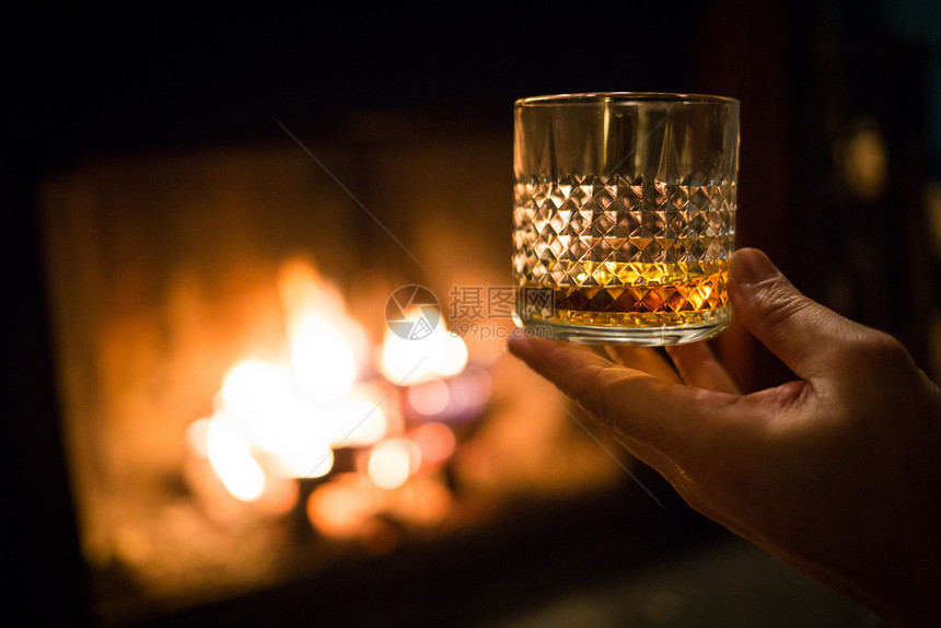 富有的浪漫难手握着威士忌杯子在温暖的壁炉上手握着威士忌杯子在壁炉上图片