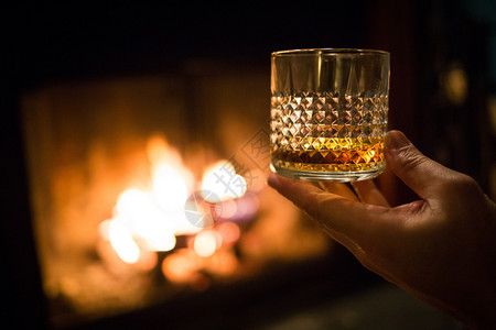 富有的浪漫难手握着威士忌杯子在温暖的壁炉上手握着威士忌杯子在壁炉上金的高清图片素材