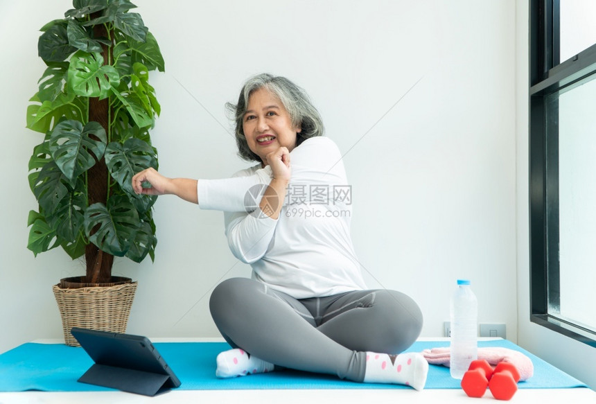尽管白色的上笔记本电脑在线课程的亚洲老年妇女在家中起居室练习时观看膝上型计算机在线课程网上锻炼培训概念数字的图片