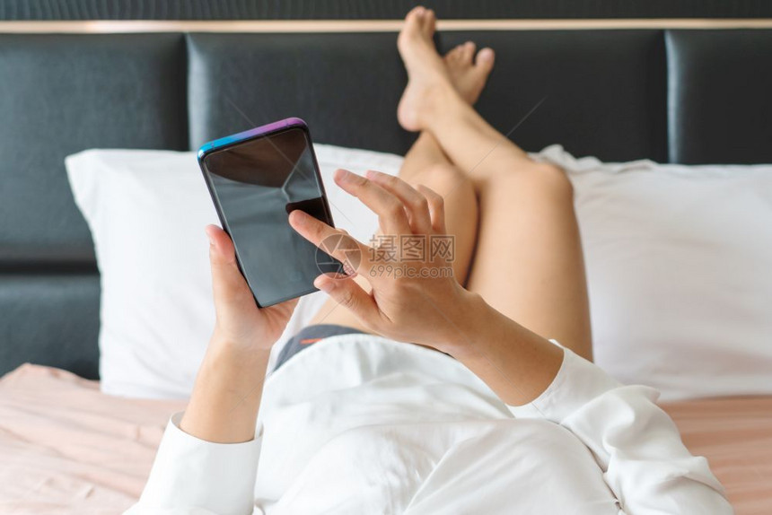 最佳尽管快乐的女子在上网时躺床用智能手机发信息腿图片