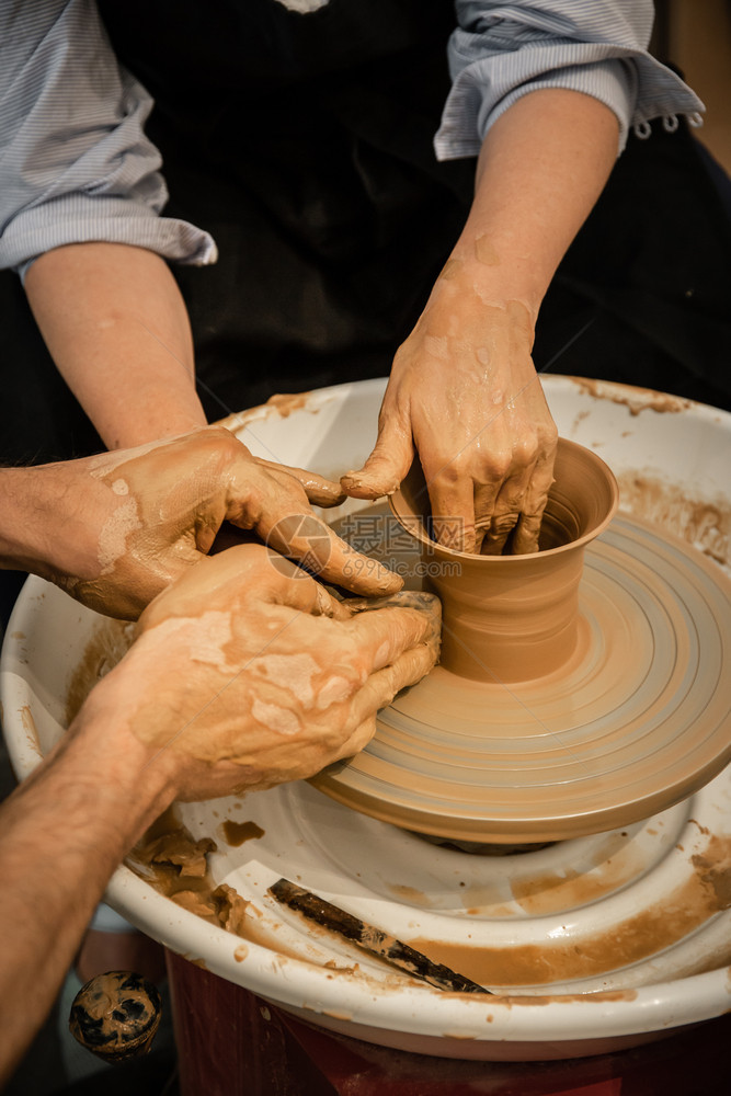 作坊专家陶器匠教女人在轮上工作脏手缝合水壶创建图片