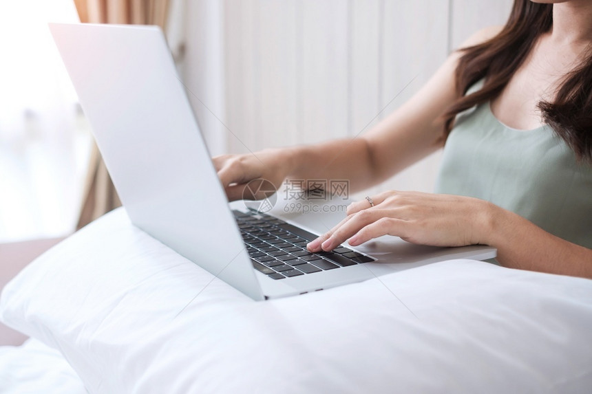 手在卧室的白枕头上坐在并使用电脑笔记本的快乐临时妇女年轻成在家工作或早上网购物自由游轮生活方式和技术概念酒店营销图片