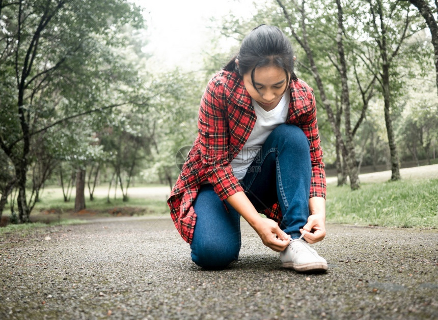 一名女游客坐在沥青上系着鞋带同时在公园自然步行度假时使用生活方式阳光健康搭售图片