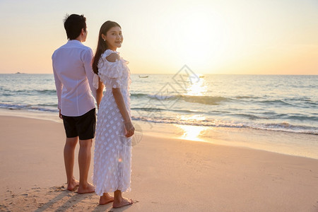 年轻的亚洲快乐情侣在海滩上握着手与一个女人面对相机鼓浪漫旅行蜜月渡暑假亚裔女和男手拥抱户外的日落背景晴天一种喜悦约会高清图片素材