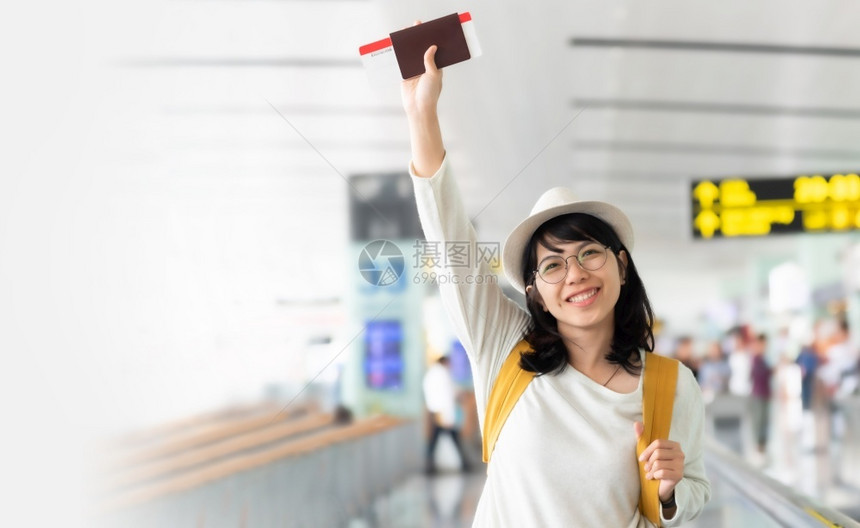快乐的亚洲妇女戴着眼镜黄色背包帽子持有飞行机票在场大厅领取护照笑一愉快登机飞
