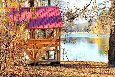 木头叶子一个简单的木护林员配有一张桌和野餐长椅红色屋顶由金属侧面制成在温暖秋天森林湖附近落叶的背景下户外活动复制WoodenAr材料高清图片素材