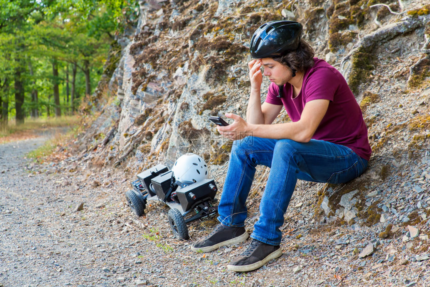 爱好骑发动机坐在有山板和手机的岩石上年轻caucasian男子图片