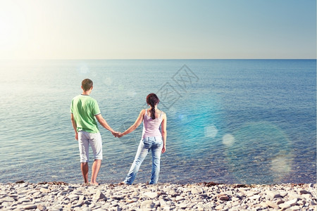 晴天女年轻夫妇站在水边相互抱起双臂俯视地平线从后面看镜头照明弹约会图片