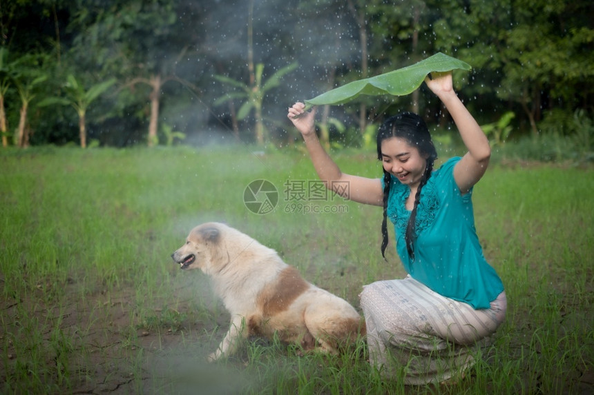 在绿花园背景下雨时一位年轻亚洲女身着香蕉叶的黑头发肖像愉快传播女孩图片