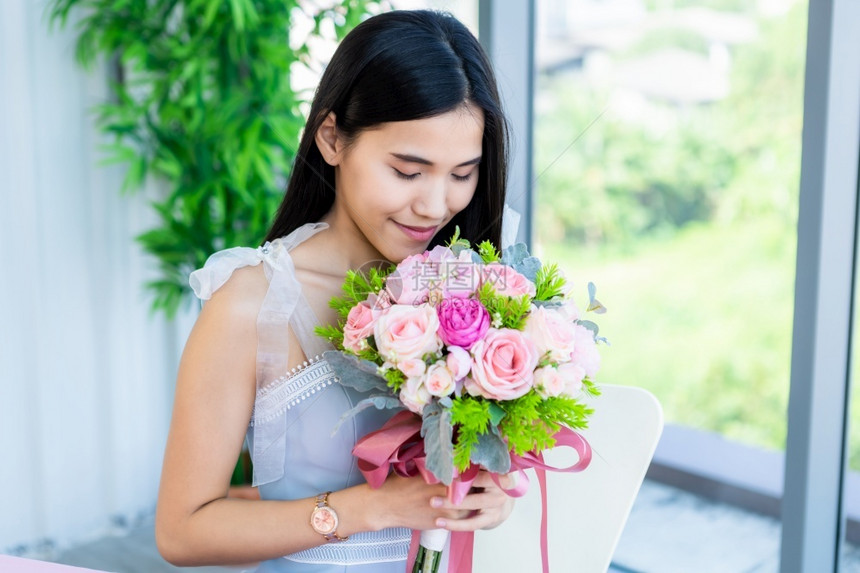 手庆典夏天情人节的概念笑亚裔年轻女坐在餐桌上吃着食物在餐厅背景中拿着一束玫瑰花朵的欢乐快图片