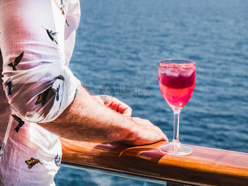 成人饮料在蓝海浪背景下游轮露天甲板上盛着一杯美丽的粉红葡萄酒时装男子侧观特近休闲和旅行概念暇和旅游概念持有美丽粉红葡萄酒的人时髦图片
