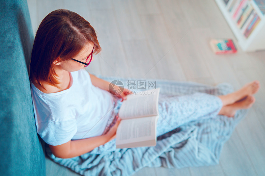 一种知识年轻美女学生在家中阅读或学习的肖像躺在床边地板上戴着有一本书的眼镜床上随意图片