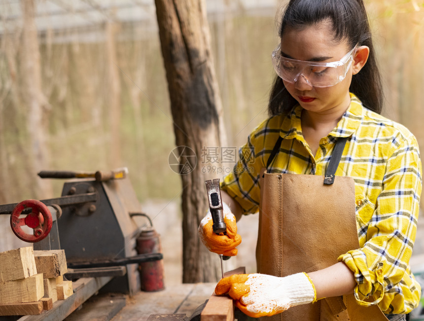 妇女站立建筑工身着经检查的衬衫在建筑工地作在木板上钉内部的木制头图片