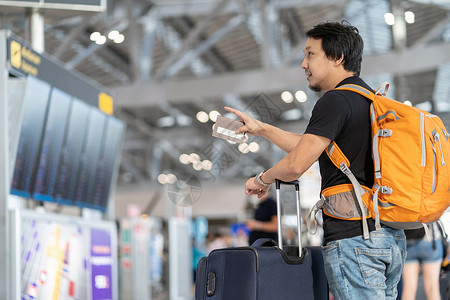 夏天休息室技术在现代机场旅行和运输概念的飞行信息屏幕上登入飞行信息屏幕时对携带行李和护照检查并指向飞行板的亚洲旅者进肖像式监视以离开高清图片素材