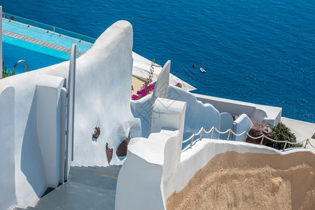 火山口外部的建筑物希腊圣托里尼岛传统楼梯到海边的卡路德拉白色墙壁蓝泳池边缘和一棵花丛露出鲜桑托里尼白楼之间通往海洋的传统楼梯在圣背景图片