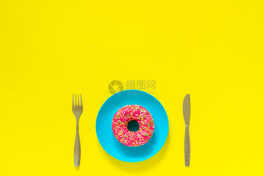 糖果粉红甜圈放在蓝色板上餐具桌刀叉子在黄底背景上保留生命复制空间顶端视图平面看不吃白日粉红甜圈放在蓝色盘子上餐具刀叉放在黄色背景图片