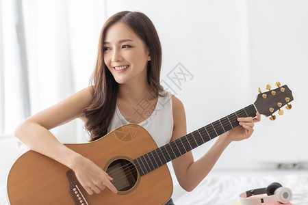 房间人们美丽无忧虑的漂亮亚洲女正在练习听声吉他快乐微笑女孩享受器在家中白间玩乐器艺术家高清图片素材