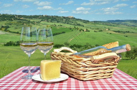 柴金白葡萄酒奶酪和面包在彩布上与意大利的托斯卡纳风景对抗蓝色的饮料图片