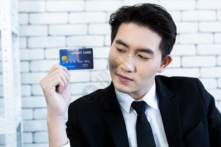 空白的男人支付亚洲英俊的年轻商人展示持有一张信用卡躺在桌子上坐办公室的白墙背景中手指高清图片素材