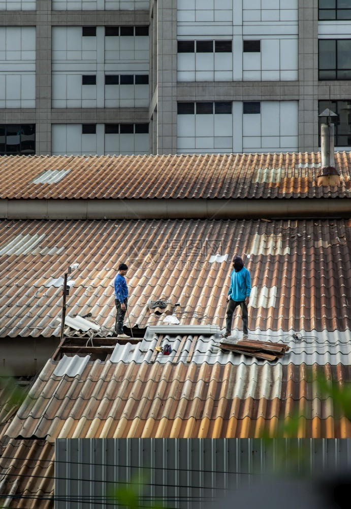 爬承包商装修泰国曼谷201年5月8日两名打杂工人在被损坏的工厂屋顶上修理瓷砖图片
