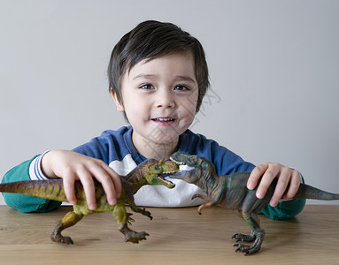 手举牌子小男孩嘴头发在家木桌边玩恐龙具的活生小男孩快乐子与他两只恐龙一起玩乐为他的放松时光而奋斗孩子的发展和想象概念儿童发展和想象力相机背景