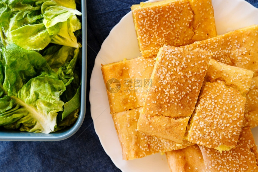 吃桌子树叶玉米面包松饼的顶端景色在蓝碗桌边面上用芝麻种子覆盖的白盘中新鲜绿色沙拉有机素食品图片