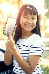 购物年轻亚洲人展示智能电话屏幕的白和笑牙般脸快乐情绪互联网快乐的图片