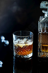 黑色的一杯威士忌或波旁在黑石桌上加冰一杯的威士忌和一个方形醒酒器一杯苏格兰威士忌和冰优质的结石背景图片