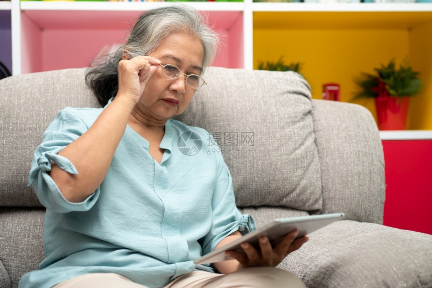 活的亚洲人在室内高级亚洲妇女戴眼镜在家沙发上放松并使用平板电脑阅读新闻和子书老年人技术概念为老年人提供技术概念图片