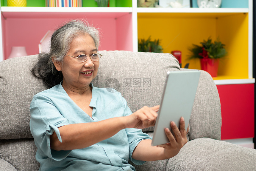 高级亚洲妇女戴眼镜在家沙发上放松并使用平板电脑阅读新闻和子书老年人技术概念为老年人提供技术概念成熟亚洲人联系图片