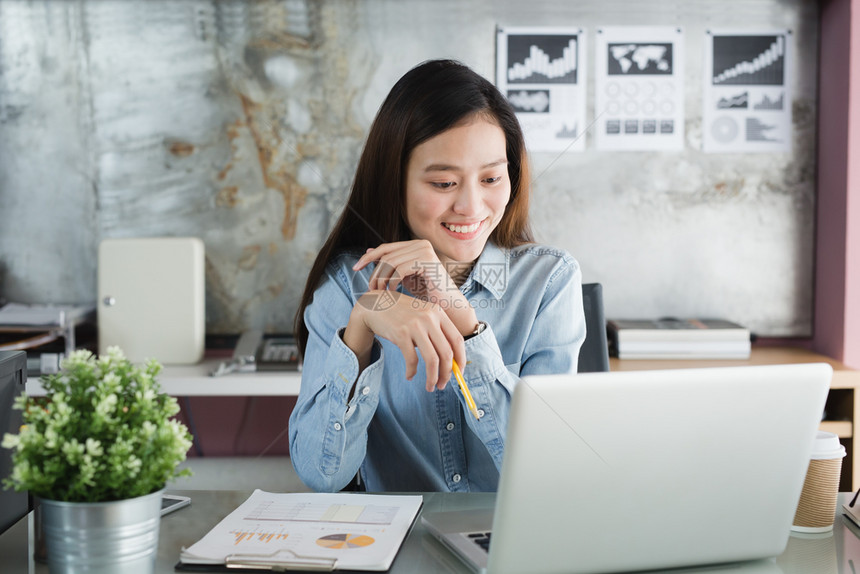 商业秘书淑女在办公室使用笔记本电脑的新一代亚洲女商人妇在努力制定移动办公室概念时微笑地坐着容图片