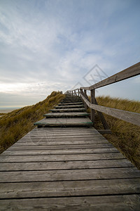 鲁路修旅行北弗里西安群岛德国施勒苏益格荷尔斯泰因在一片阴云的天里带楼梯或木板走的质道路穿过安鲁姆山顶的沙丘景观和新生活阿姆鲁地平线背景