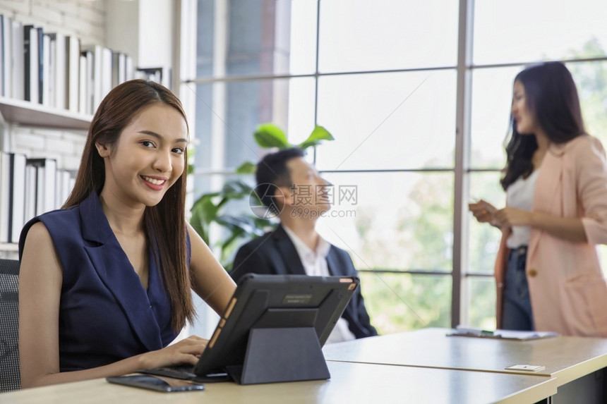 商业妇女使用现代数字平板电脑而同事在办公室团队工作会议和伙伴关系概念的背景中进行互动女商人使用现代数字片应程序沟通木板图片