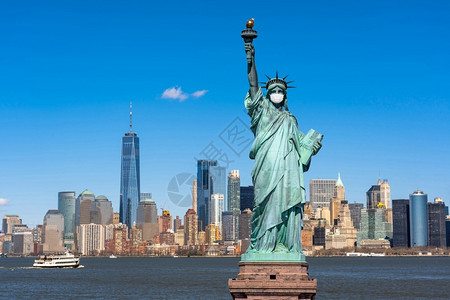 在纽约市自由女神像戴外科面具当时Covid19在纽约克市风景河边联合州冠状流行建筑和上发生爆炸并带有旅游概念建筑学天空曼哈顿背景