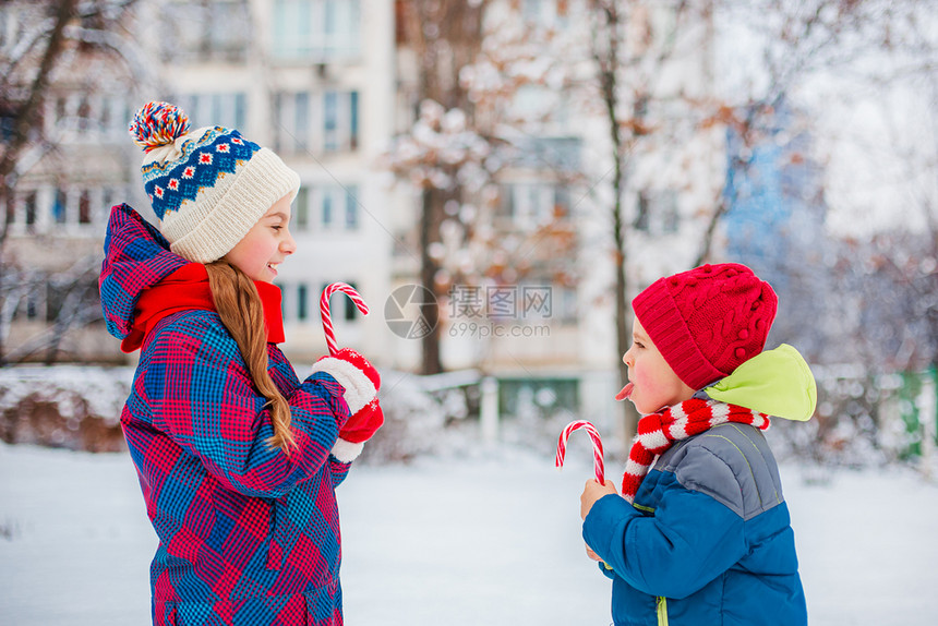 十二月灯一个女孩和男在冬天的街道上手里拿着圣诞糖果的肖像兄弟姐妹在假期里玩得很开心在冬天的街道上一个女孩和男手里拿着圣诞糖果的肖图片