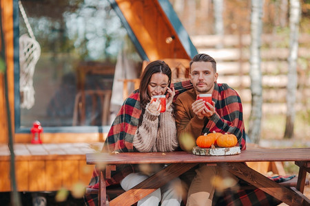 成人男喝秋天坐在木制老桌子上的年轻夫妇秋天在他们家的院子里带着咖啡因的年轻夫妇背景图片