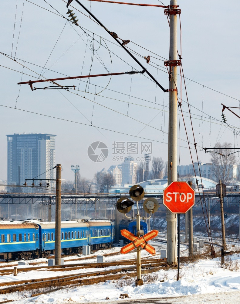 象征天空移动铁路道口的红色停车标志以铁路轨道蓝色火车厢和城市入口处的景观为背冬季城市观垂直图像城市入口处铁路道的红色停车标志以冬图片