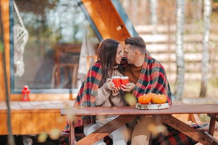 微笑年轻夫妇坐在他们家秋森林背景的木制老桌子上在秋天与咖啡因家庭院子的一对小夫妇屋情绪背景图片