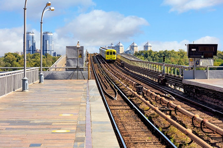 基辅一座地铁桥路轨迹的开阔部分在城市风景的背下一辆柠檬色地铁列车沿这条路横行而蓝色的天空前方则略微模糊供复制空间使用地铁列车穿过背景
