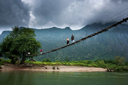 生活一群老挝高中女生穿过南宋河上简单的悬吊脚桥在北老挝农村背景的山上云雾笼罩着巨大黑暗位于北老挝农村地区运输旅行背景图片