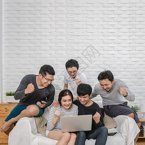 情侣行动毛笔字东南数字的屋坐在并使用数码笔记本电脑的亚洲快乐人群在现代家庭客厅沙发上欢乐和庆祝行动夫妇成功和生活方式概念上坐着背景