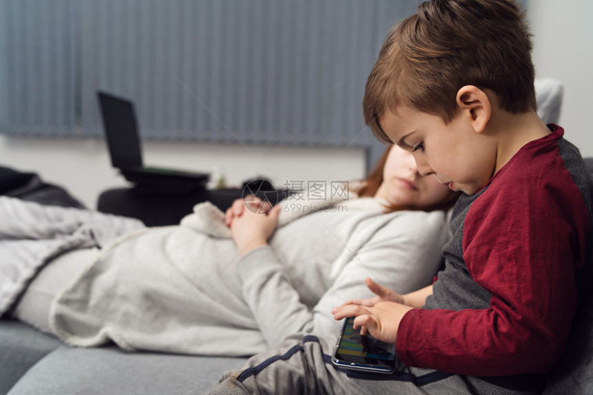 父母移动的甜睡在沙发上或床玩游戏手机智能电话或在隔离期间晚上家打视频电话的Caucasiansian男孩小妈和儿子的侧边视图图片