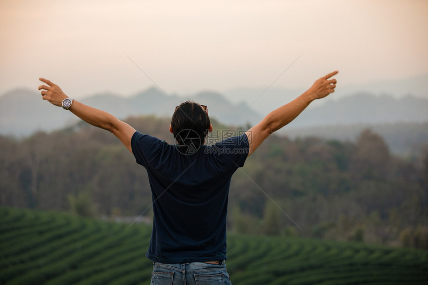 自由旅行者男子与举起的手站在一享受着美丽的自然在日落时欢呼年轻节假日概念旅行时间不长徒步旅行者亚洲人轮廓图片