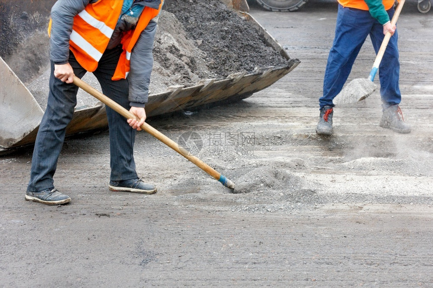 老的加载身穿明橙色反射背心的公路工人正在修复旧路将道残块铲入一个平板桶复制空间道路工人清理从被毁坏的沥青中清扫道路将其装入平板桶图片
